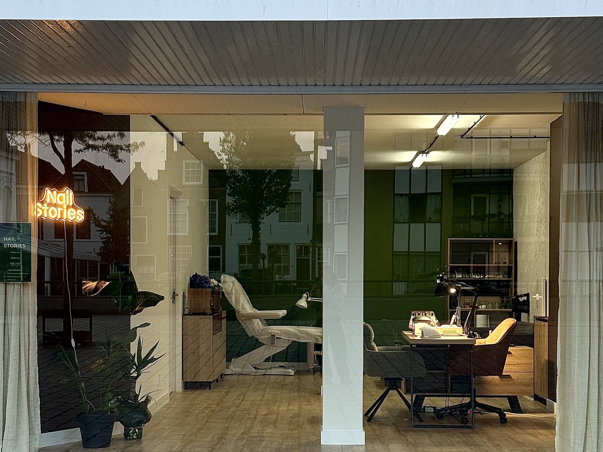 De etalage van Nail Stories met het neonbord, de behandelstoel en de werktafel